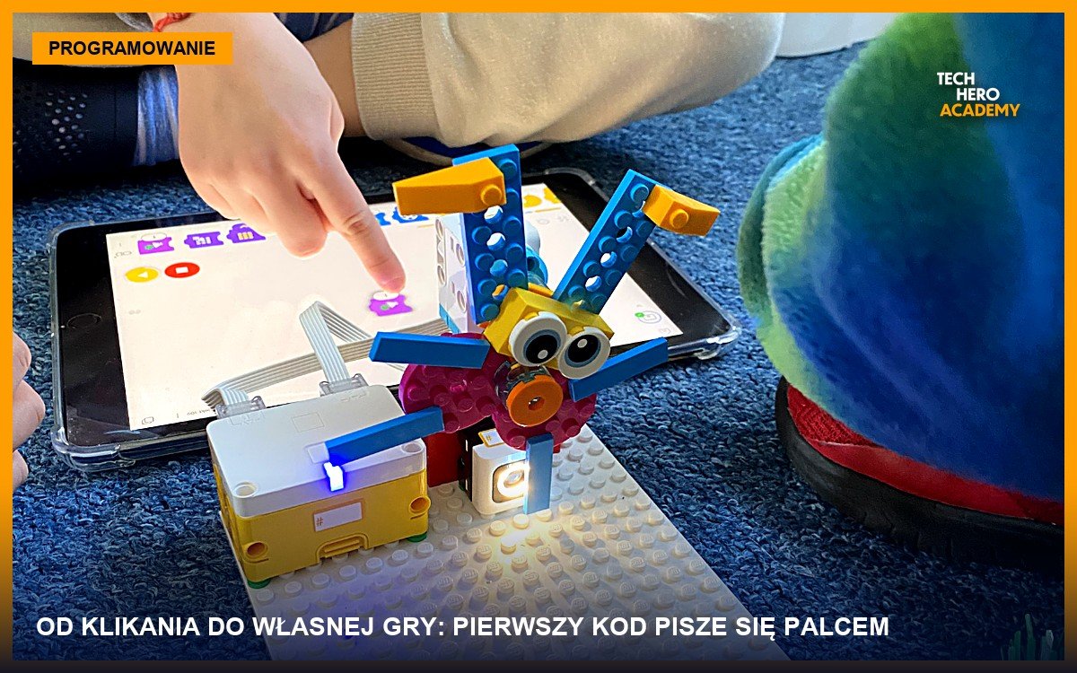 Dziecko wskazuje palcem kod blokowy na ekranie tabletu, obok robot zbudowany z klocków LEGO na zajęciach Tech Hero Academy