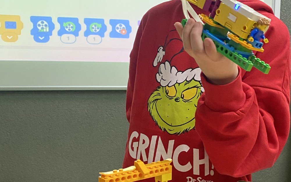 Zajęcia Tech Hero Academy: program ułożony z kolorowych bloków na ekranie projektora i model z klocków LEGO trzymany przez dziecko