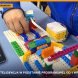 Uczeń buduje przy stole model z klocków LEGO z modułem elektronicznym, obok tablet z aplikacją do programowania blokowego