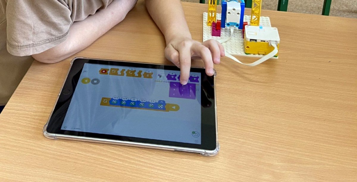 Zajęcia Tech Hero Academy: dziecko układa program z kolorowych bloków na tablecie, obok robot zbudowany z klocków LEGO