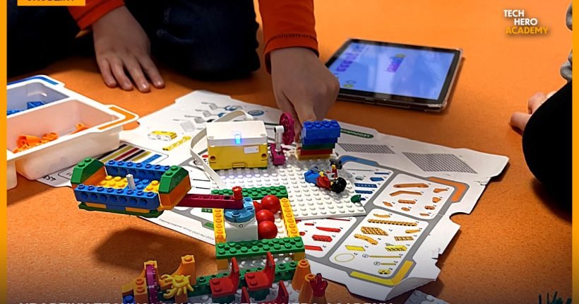 Dzieci na podłodze budują konstrukcje z klocków LEGO i programują je na tablecie podczas urodzin technologicznych w Tech Hero Academy